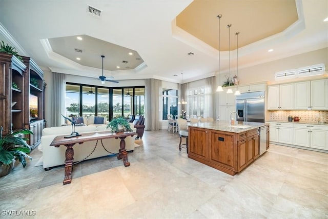 kitchen featuring light stone countertops, appliances with stainless steel finishes, a tray ceiling, a kitchen island with sink, and pendant lighting