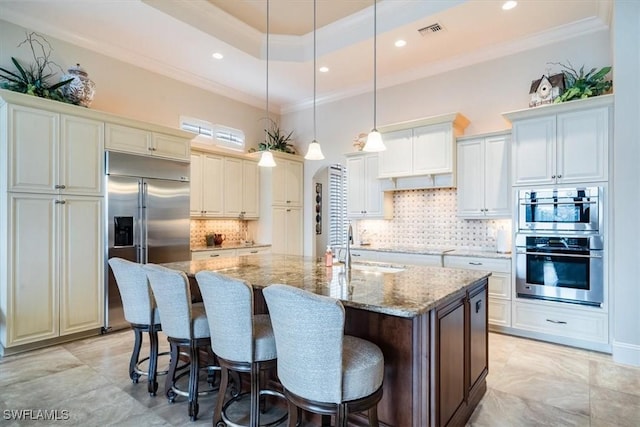 kitchen with light stone countertops, a kitchen breakfast bar, stainless steel appliances, pendant lighting, and an island with sink