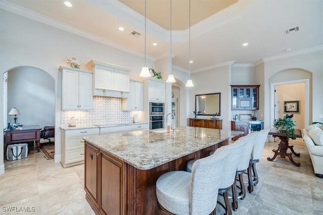 kitchen featuring pendant lighting, backsplash, a spacious island, light stone counters, and white cabinetry