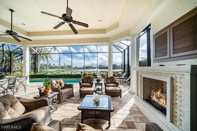 sunroom / solarium featuring a tray ceiling, ceiling fan, and an outdoor fireplace