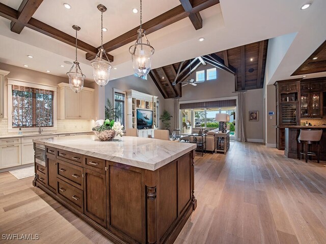 kitchen with backsplash, a spacious island, beamed ceiling, decorative light fixtures, and light hardwood / wood-style floors