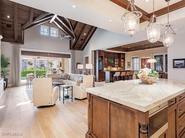 kitchen featuring open floor plan, light stone counters, beamed ceiling, and pendant lighting