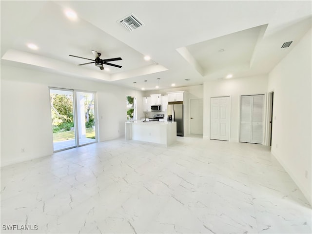 unfurnished living room featuring ceiling fan and a raised ceiling