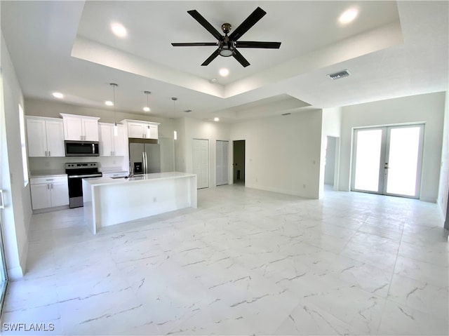 kitchen featuring appliances with stainless steel finishes, french doors, a tray ceiling, white cabinets, and an island with sink