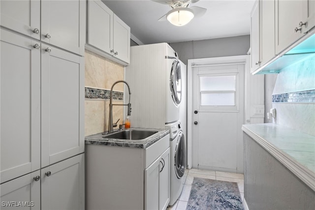 washroom featuring ceiling fan, sink, stacked washing maching and dryer, cabinets, and light tile patterned flooring