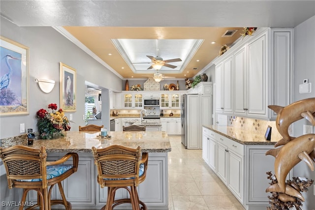 kitchen featuring white cabinetry, light stone countertops, stainless steel appliances, kitchen peninsula, and a breakfast bar area