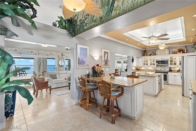 kitchen featuring light stone countertops, appliances with stainless steel finishes, a kitchen island with sink, a water view, and white cabinets