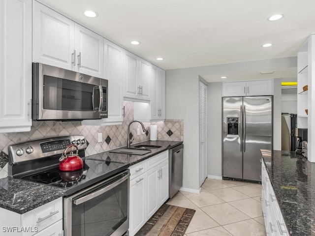 kitchen featuring appliances with stainless steel finishes, sink, light tile patterned floors, dark stone countertops, and white cabinets