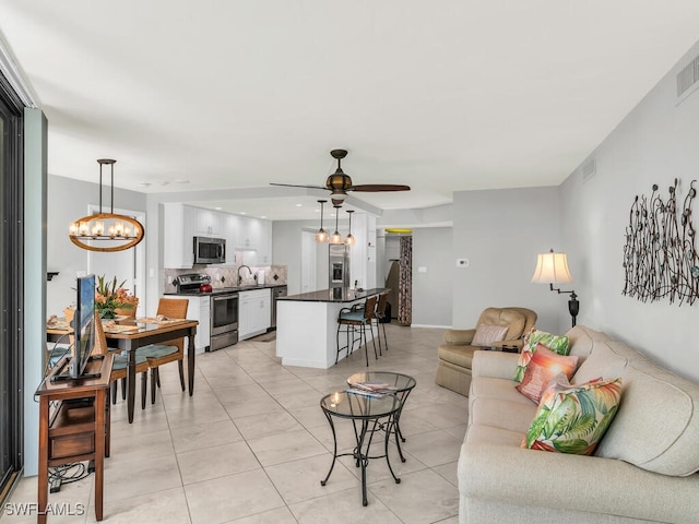 living room with light tile patterned floors, ceiling fan with notable chandelier, and sink