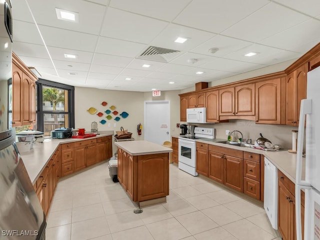 kitchen with light tile patterned floors, white appliances, a kitchen island, and a drop ceiling