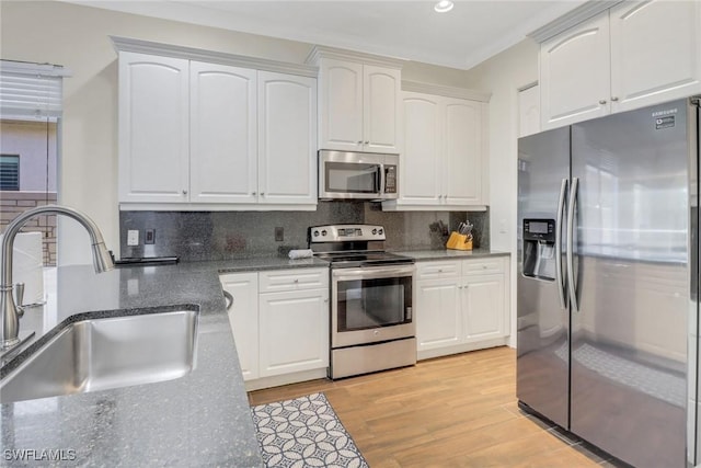 kitchen with stainless steel appliances, backsplash, white cabinets, a sink, and light wood-type flooring