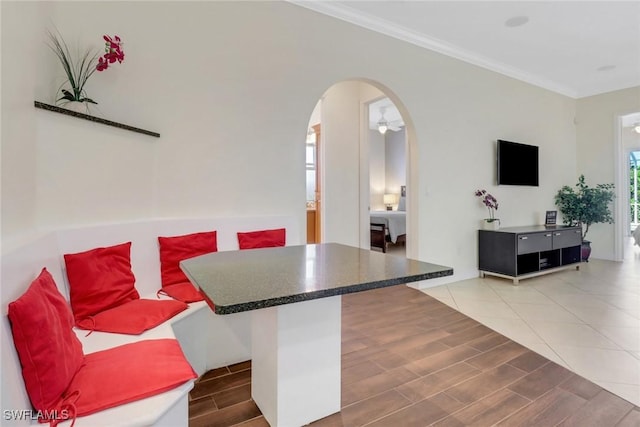 kitchen featuring arched walkways, wood finish floors, dark countertops, ornamental molding, and a kitchen bar