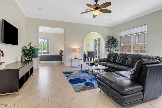 living room with arched walkways, light tile patterned flooring, a ceiling fan, and crown molding