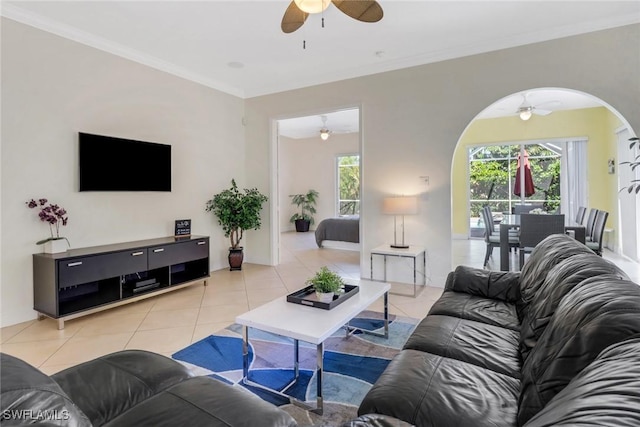 living area featuring light tile patterned floors, ceiling fan, ornamental molding, and arched walkways