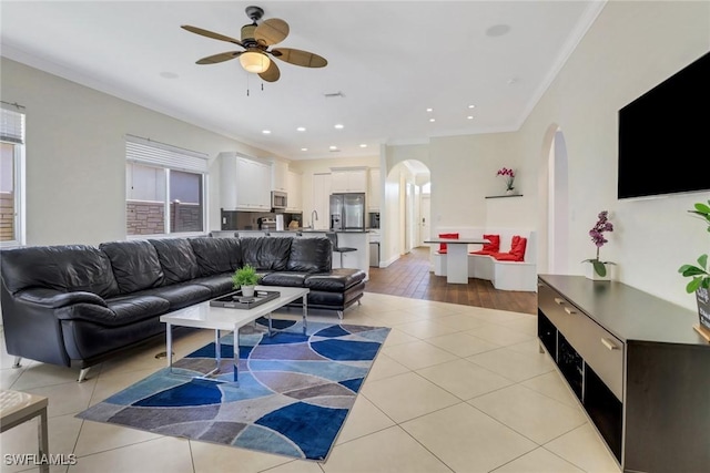 living area with arched walkways, ceiling fan, light tile patterned floors, recessed lighting, and ornamental molding