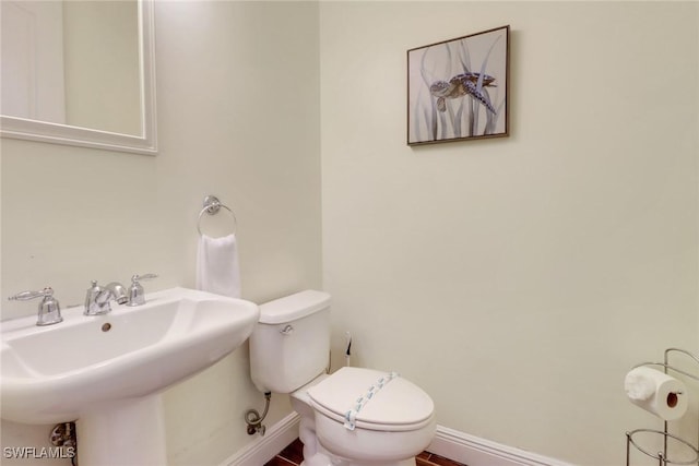 half bath with a sink, toilet, and baseboards