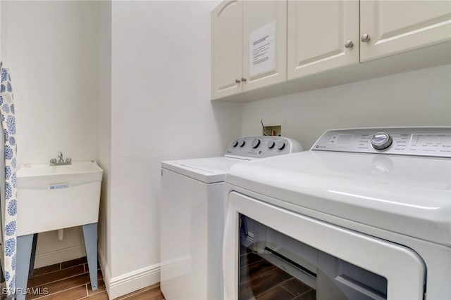 clothes washing area featuring wood finish floors, washer and clothes dryer, cabinet space, and baseboards