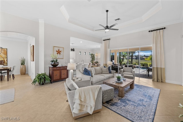 tiled living room featuring a tray ceiling, crown molding, and ceiling fan