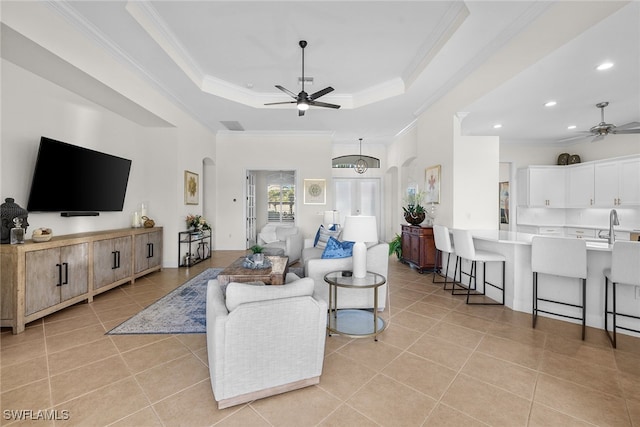 tiled living room featuring sink, ceiling fan, a raised ceiling, and crown molding