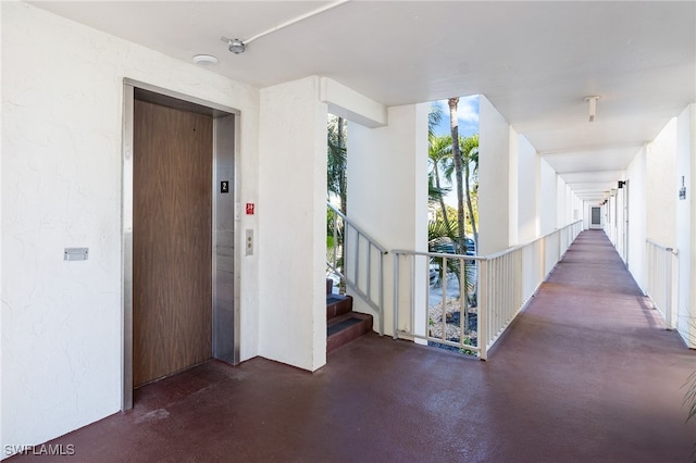 hallway with finished concrete flooring, a textured wall, elevator, stairs, and floor to ceiling windows