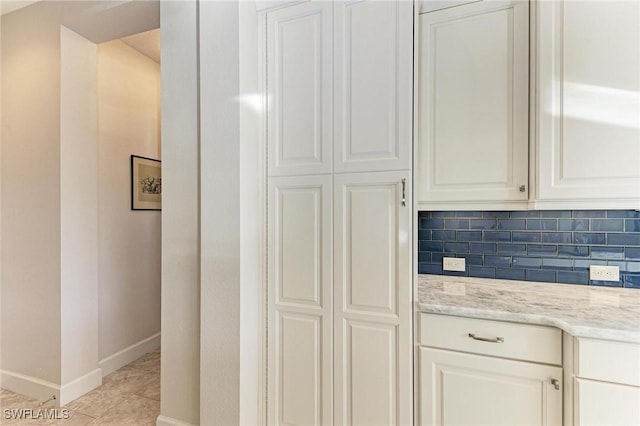 kitchen with white cabinetry, light tile patterned floors, light stone counters, and decorative backsplash