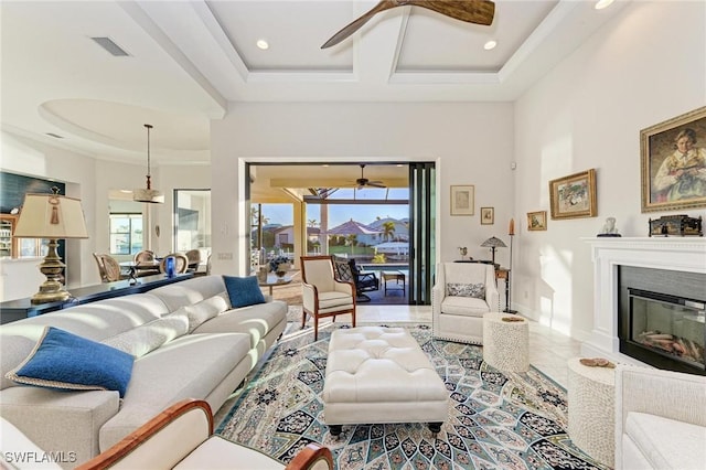 living room with a towering ceiling, coffered ceiling, ceiling fan, a high end fireplace, and a raised ceiling