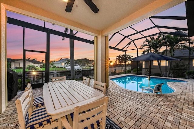 pool at dusk featuring a water view, ceiling fan, a patio, and glass enclosure