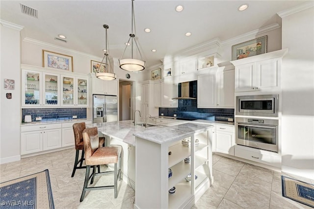 kitchen with appliances with stainless steel finishes, a kitchen island with sink, light stone countertops, white cabinets, and wall chimney exhaust hood