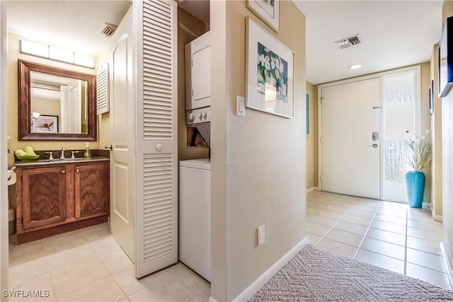 hall featuring light tile patterned floors, stacked washer and dryer, and sink