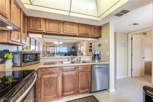 kitchen with sink, wall chimney exhaust hood, light tile patterned floors, appliances with stainless steel finishes, and a notable chandelier