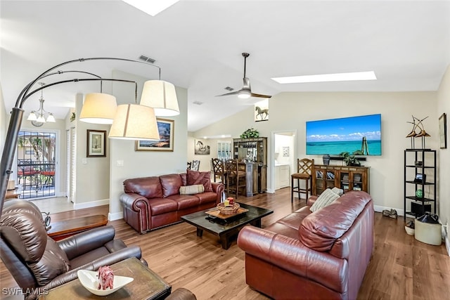 living room featuring vaulted ceiling with skylight, wood-type flooring, and ceiling fan with notable chandelier