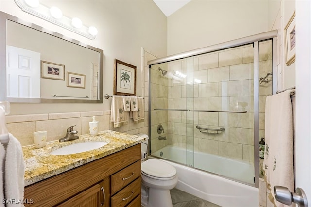 full bathroom featuring vanity, tile patterned floors, bath / shower combo with glass door, toilet, and tile walls