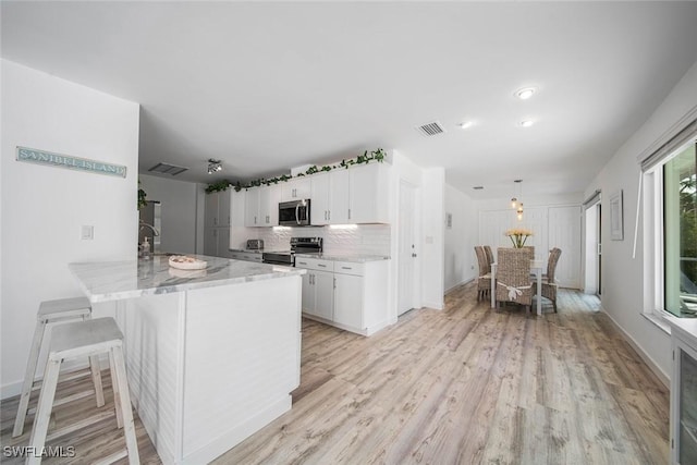 kitchen featuring white cabinetry, a kitchen breakfast bar, light hardwood / wood-style flooring, kitchen peninsula, and appliances with stainless steel finishes