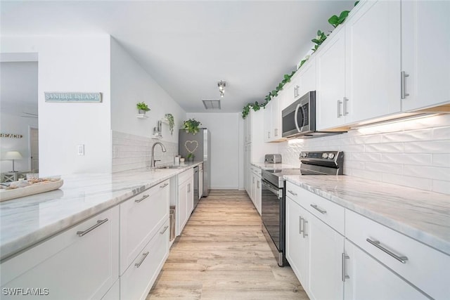 kitchen featuring white cabinets, light stone counters, light wood-type flooring, and appliances with stainless steel finishes