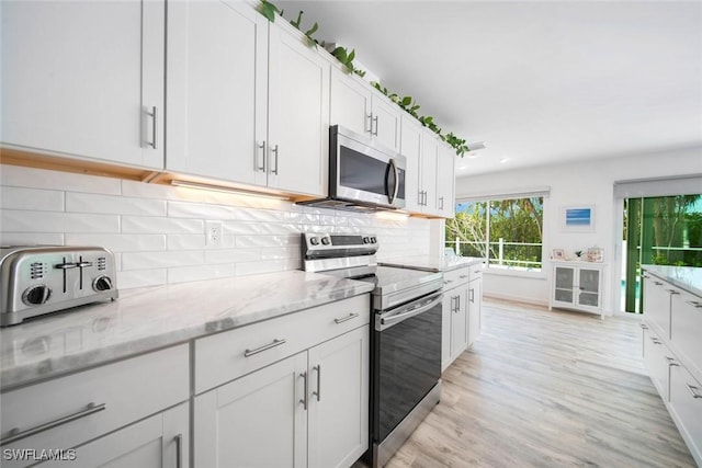 kitchen with light stone countertops, decorative backsplash, light wood-type flooring, stainless steel appliances, and white cabinetry