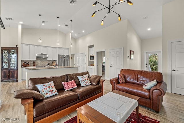 living room featuring a notable chandelier, light hardwood / wood-style floors, and high vaulted ceiling