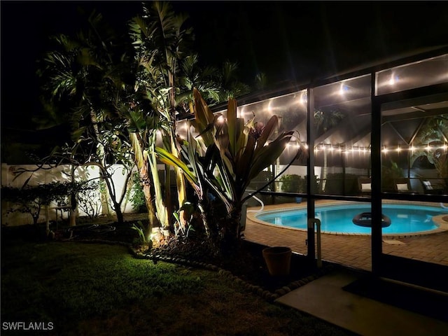 pool at night featuring a lanai and a patio area