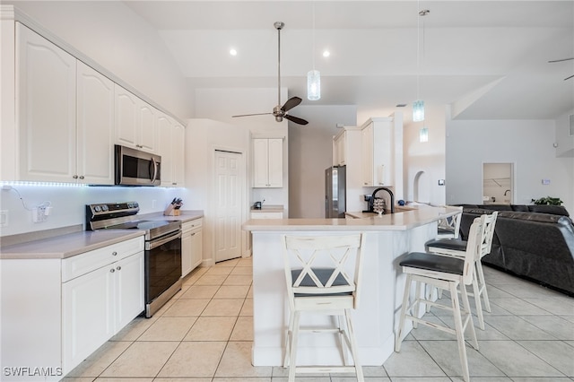 kitchen with a kitchen bar, decorative light fixtures, light tile patterned floors, appliances with stainless steel finishes, and white cabinets