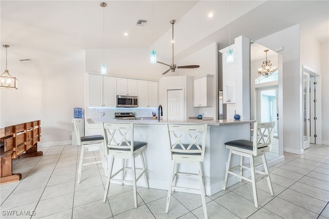 kitchen featuring appliances with stainless steel finishes, a breakfast bar, pendant lighting, ceiling fan with notable chandelier, and white cabinetry