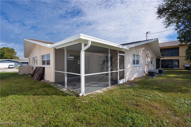 rear view of house featuring a sunroom, central AC, and a lawn