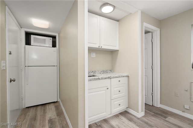 kitchen with light stone countertops, white cabinetry, light wood-type flooring, and white appliances