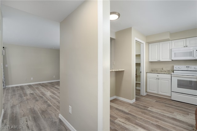 kitchen featuring white cabinets, light stone countertops, light wood-type flooring, and white appliances