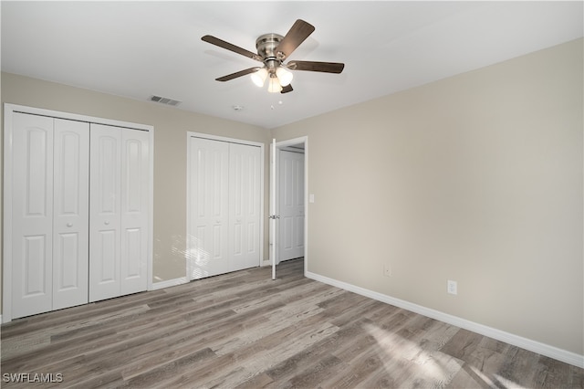 unfurnished bedroom with light wood-type flooring, ceiling fan, and multiple closets