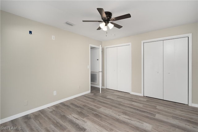 unfurnished bedroom with ceiling fan, light wood-type flooring, and multiple closets