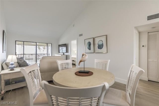 dining space with light hardwood / wood-style floors and high vaulted ceiling