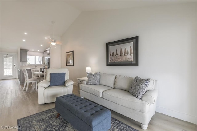 living room with ceiling fan, light hardwood / wood-style flooring, and vaulted ceiling