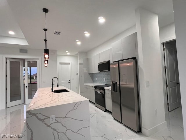 kitchen featuring light stone counters, stainless steel appliances, a kitchen island with sink, sink, and decorative light fixtures