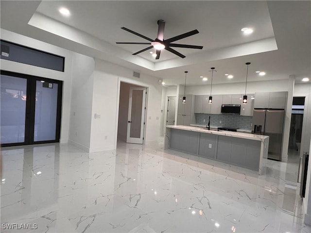 kitchen with gray cabinetry, a raised ceiling, hanging light fixtures, decorative backsplash, and appliances with stainless steel finishes