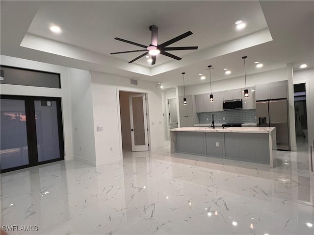 kitchen featuring a raised ceiling, gray cabinets, tasteful backsplash, decorative light fixtures, and stainless steel appliances