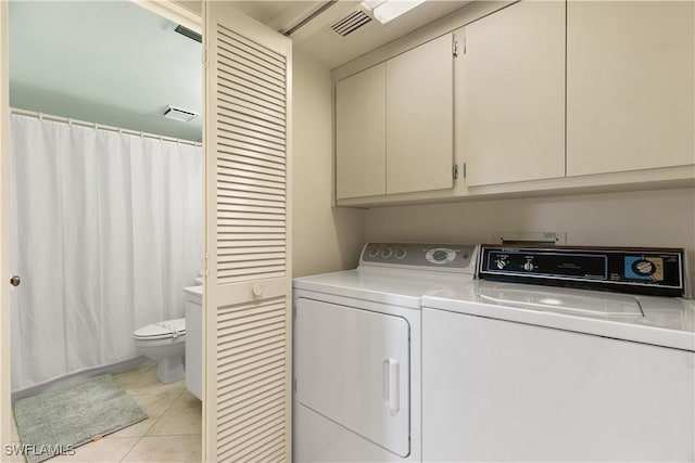 clothes washing area with light tile patterned flooring, cabinets, and washing machine and clothes dryer